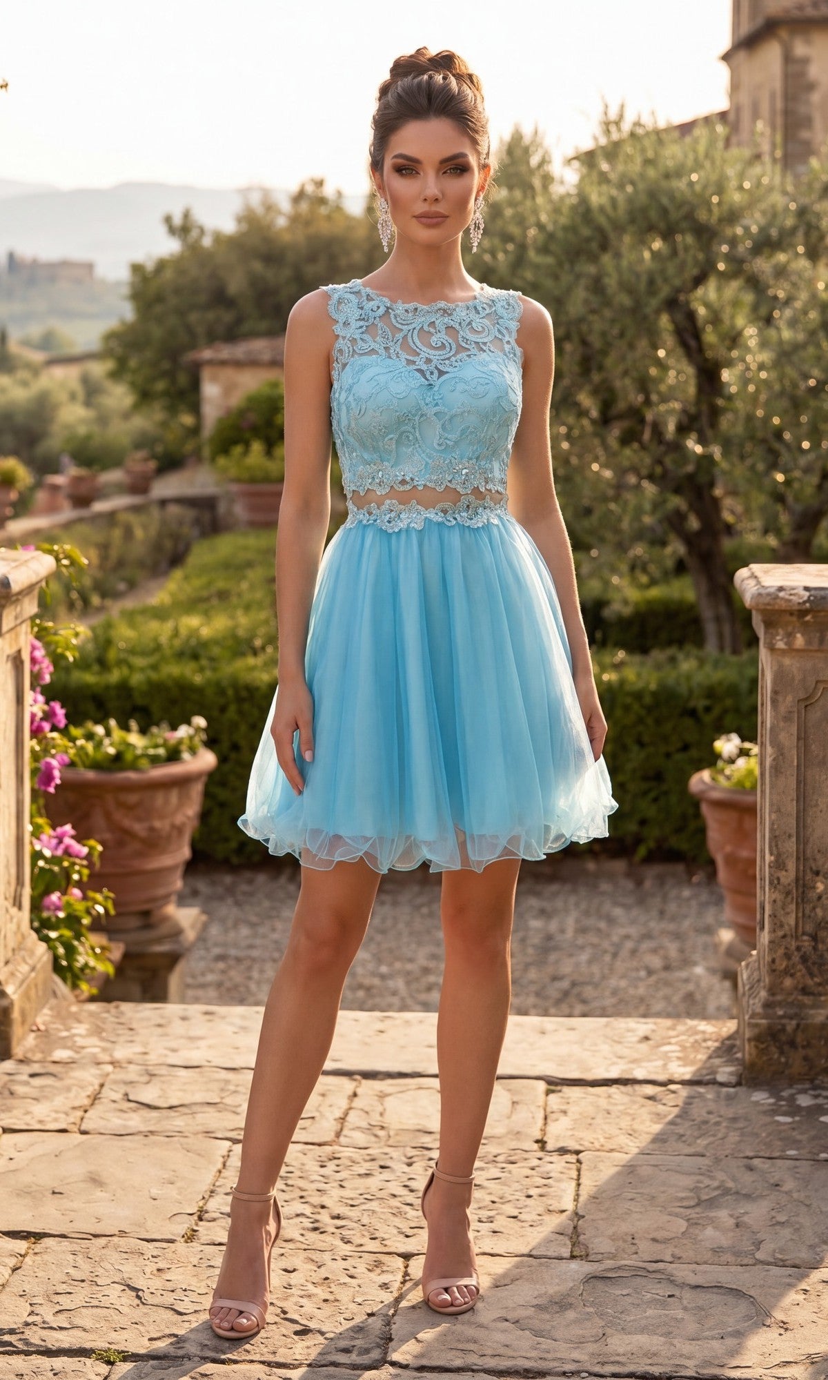 Outdoors on a stone patio surrounded by potted plants and greenery, a woman wears the Chicas C9350 Short Homecoming Dress—a light blue, sleeveless design featuring an illusion lace bodice and an elegant A-line tulle skirt—styled with nude heels.